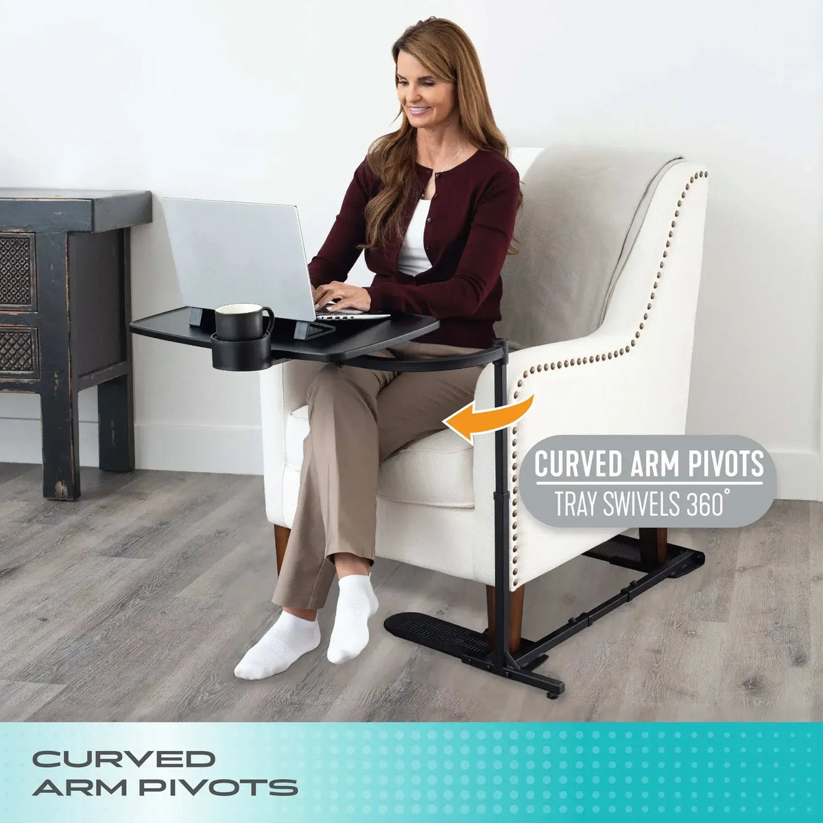 Overbed swivel tray table with curved arm pivots, shown in use by seated woman with laptop and mug on black tray surface