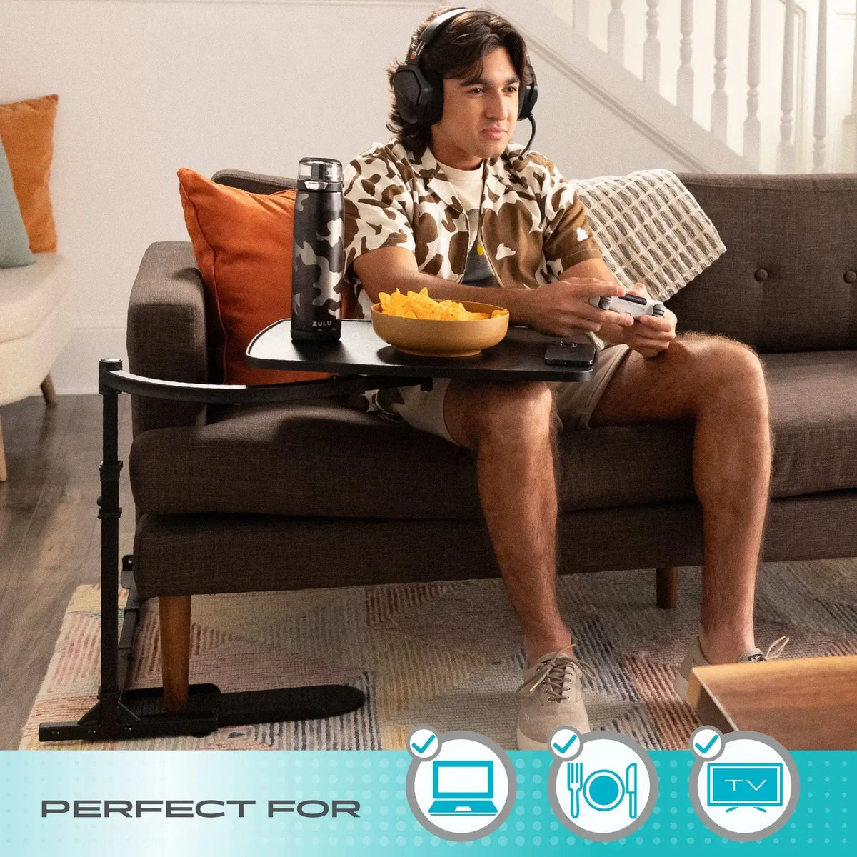 Stander Wonder Tray XL adjustable oversofa table beside man gaming on couch with snacks and water bottle on tray surface