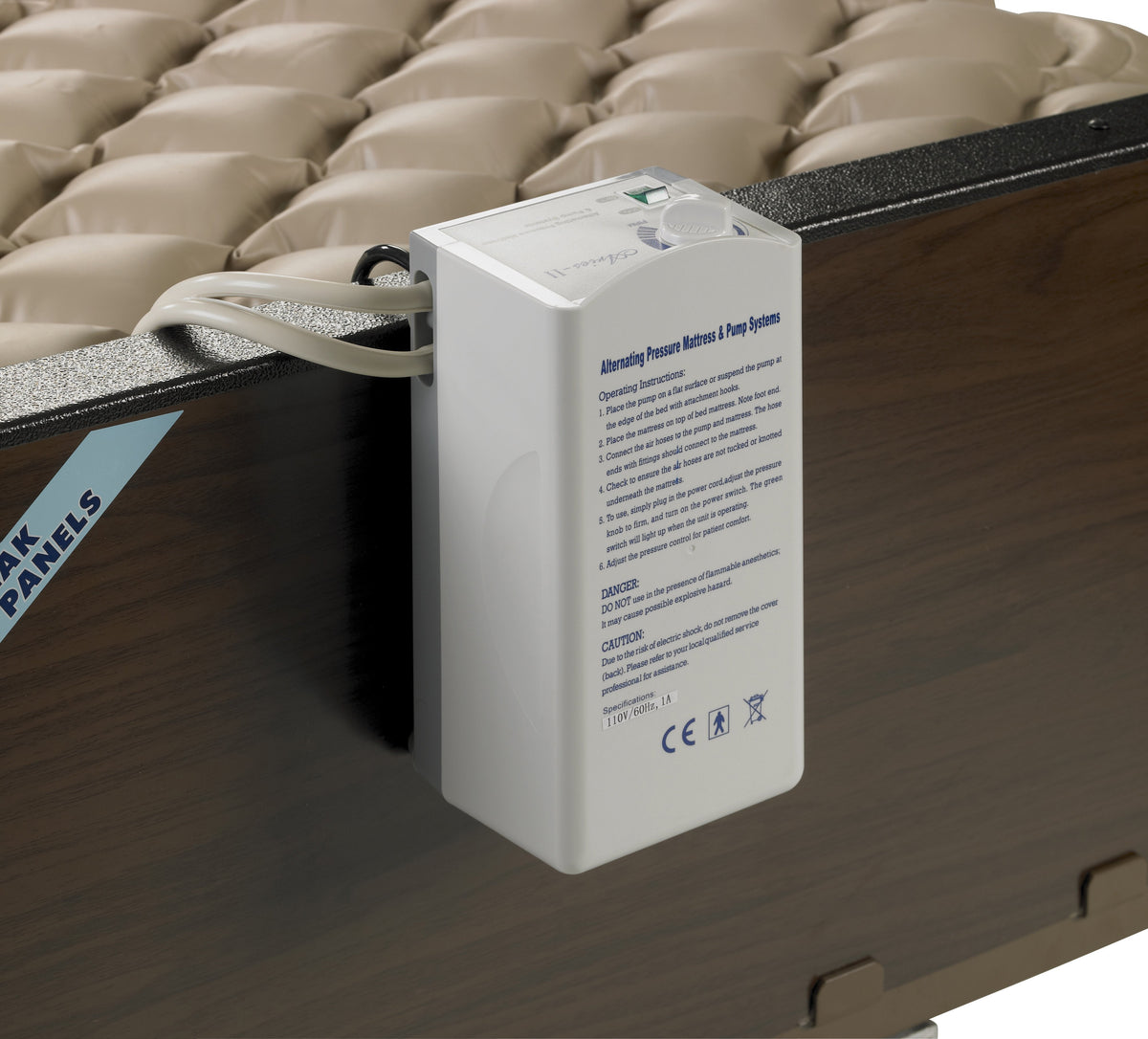 Alternating pressure pump unit mounted on bed rail beside a tan bubble-cell pressure relief mattress pad