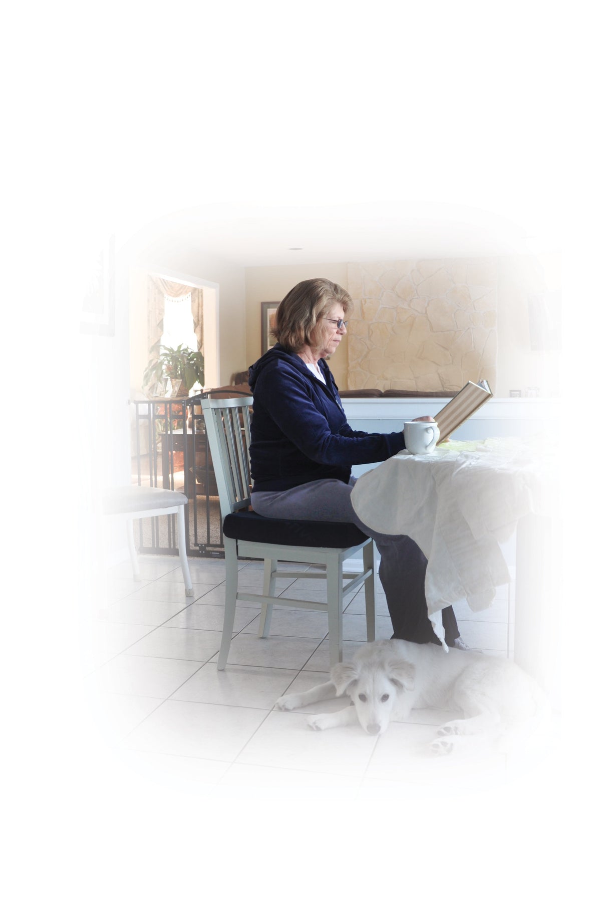 Wheelchair seat cushion in use as older woman sits reading at a dining table with a white dog resting at her feet