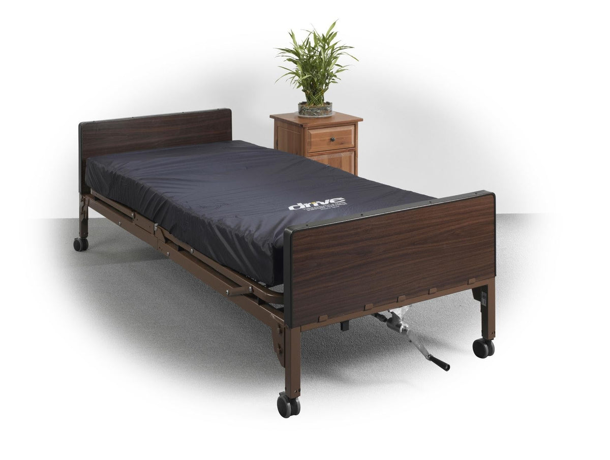 Full electric hospital bed with dark wood-finish frame, casters, head and footboards, and a dark mattress, beside a wooden