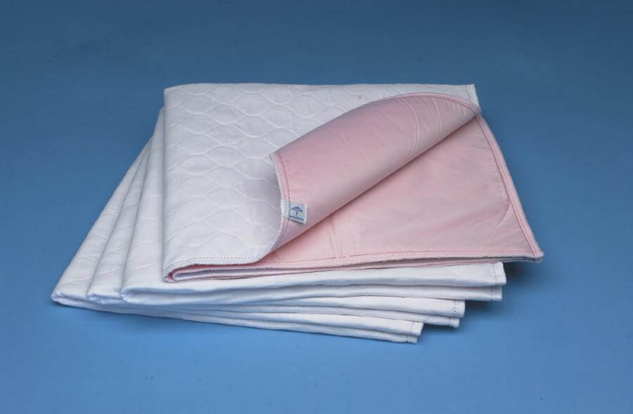 Reusable underpads stacked in a set of six, white quilted top surface with pink waterproof backing, folded and displayed on
