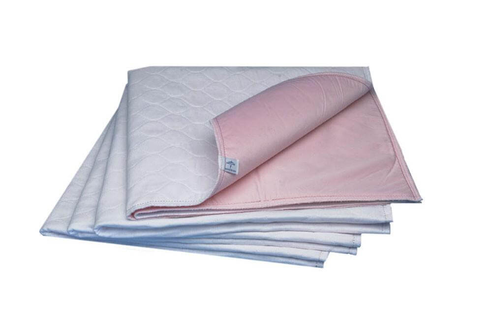 Reusable underpads stacked in a set of six, white quilted top surface with pink waterproof backing, corner folded to show
