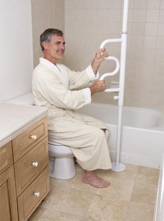 Security pole and curve grab bar with man in bathrobe seated on toilet gripping white floor-to-ceiling pole beside bathtub