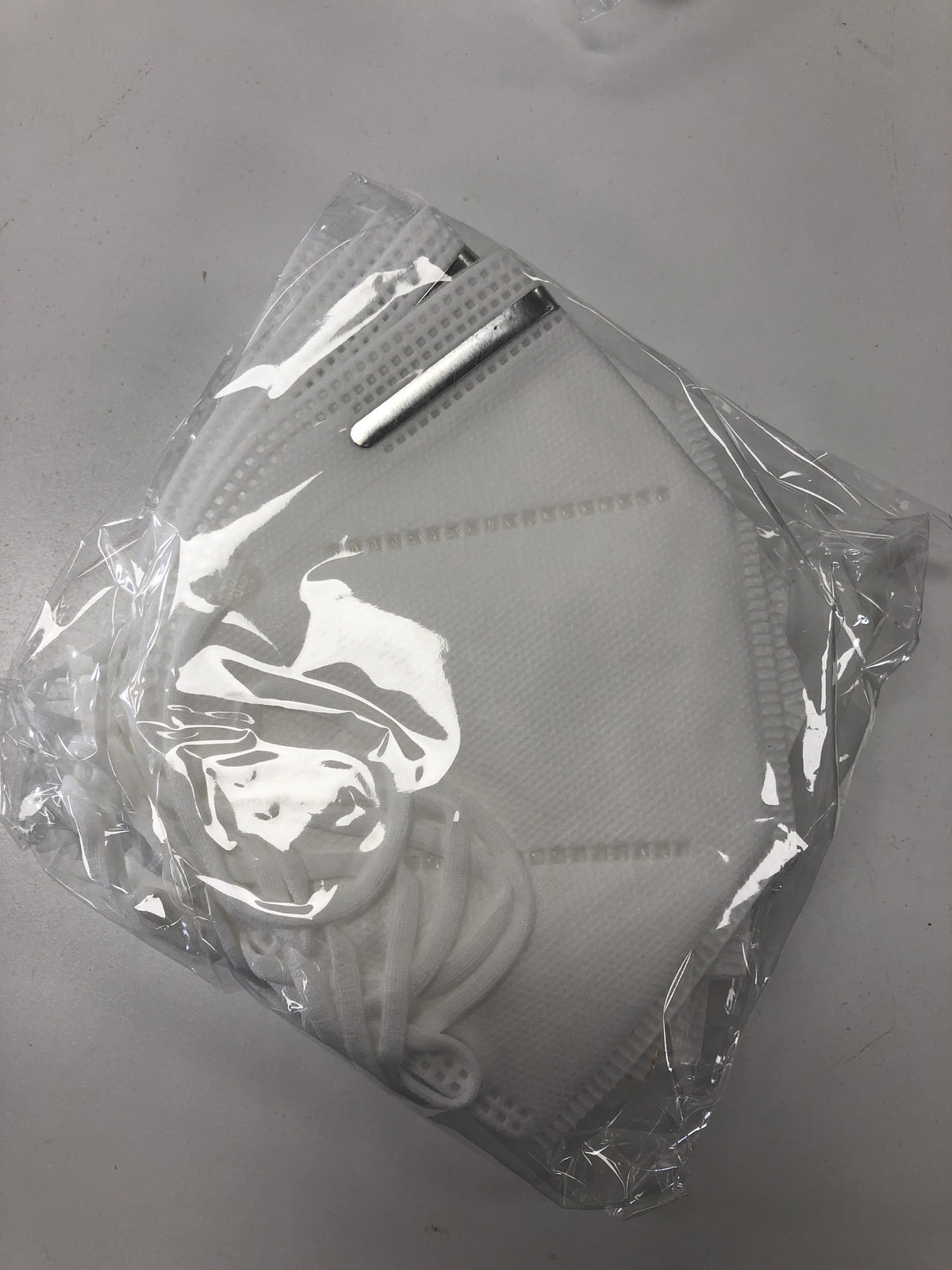 Flat-fold respirator mask with metal nose wire and ear loops, sealed in clear plastic packaging